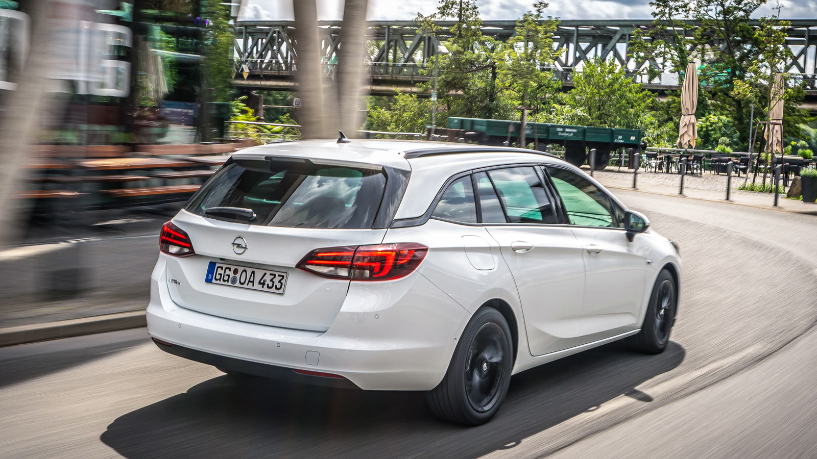 Biały Opel Astra Kombi na wirażu, szybka jazda miejska. Tylne lampy LED