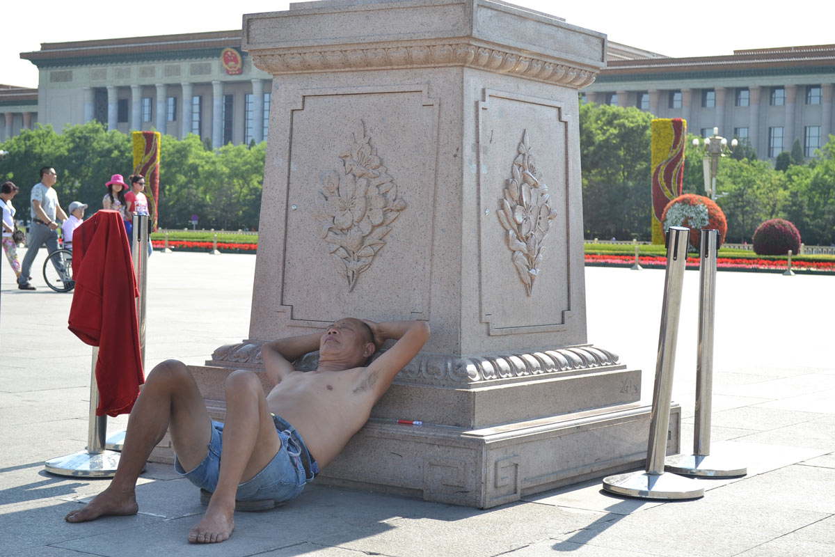 Mężczyzna drzemiący w cieniu pod monumentem w centrum Pekinu