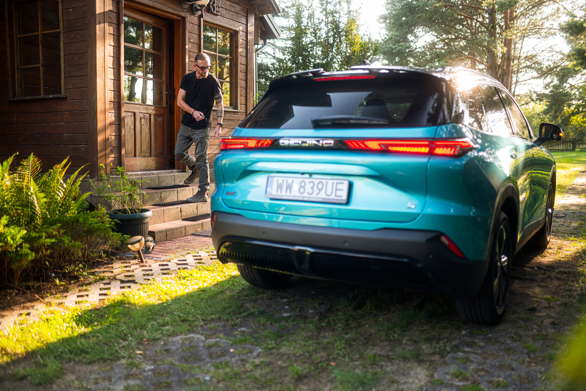 BAIC 5 Luxury błękitny metalik. Tył samochodu. Zamknięty ganek leśniczówki. Zamykanie auta pilotem, centralny zamek