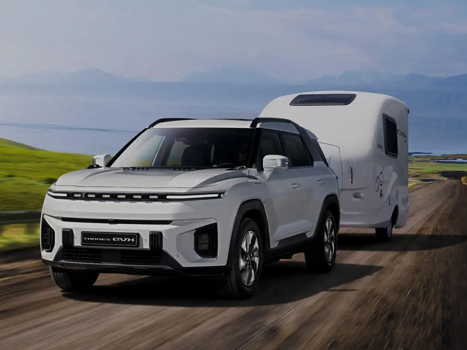 Elektryczny KGM Torres EVX ciągnie przyczepę kempingową pod górę. Otwarty pejzaż, fjord