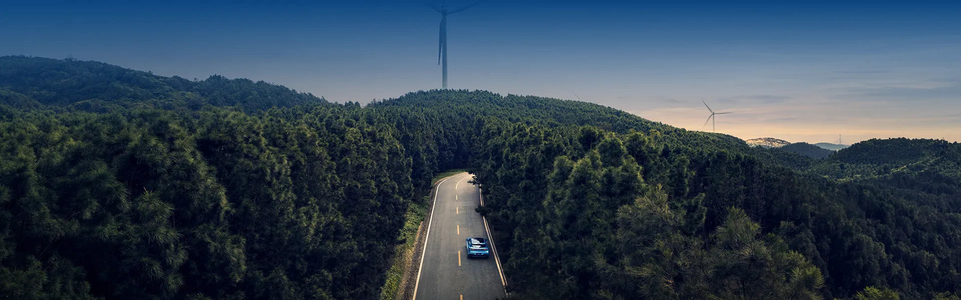 Leśna szosa w górach, wiatraki generujące prąd elektryczny. Samochód elektryczny Deepal z lotu ptaka